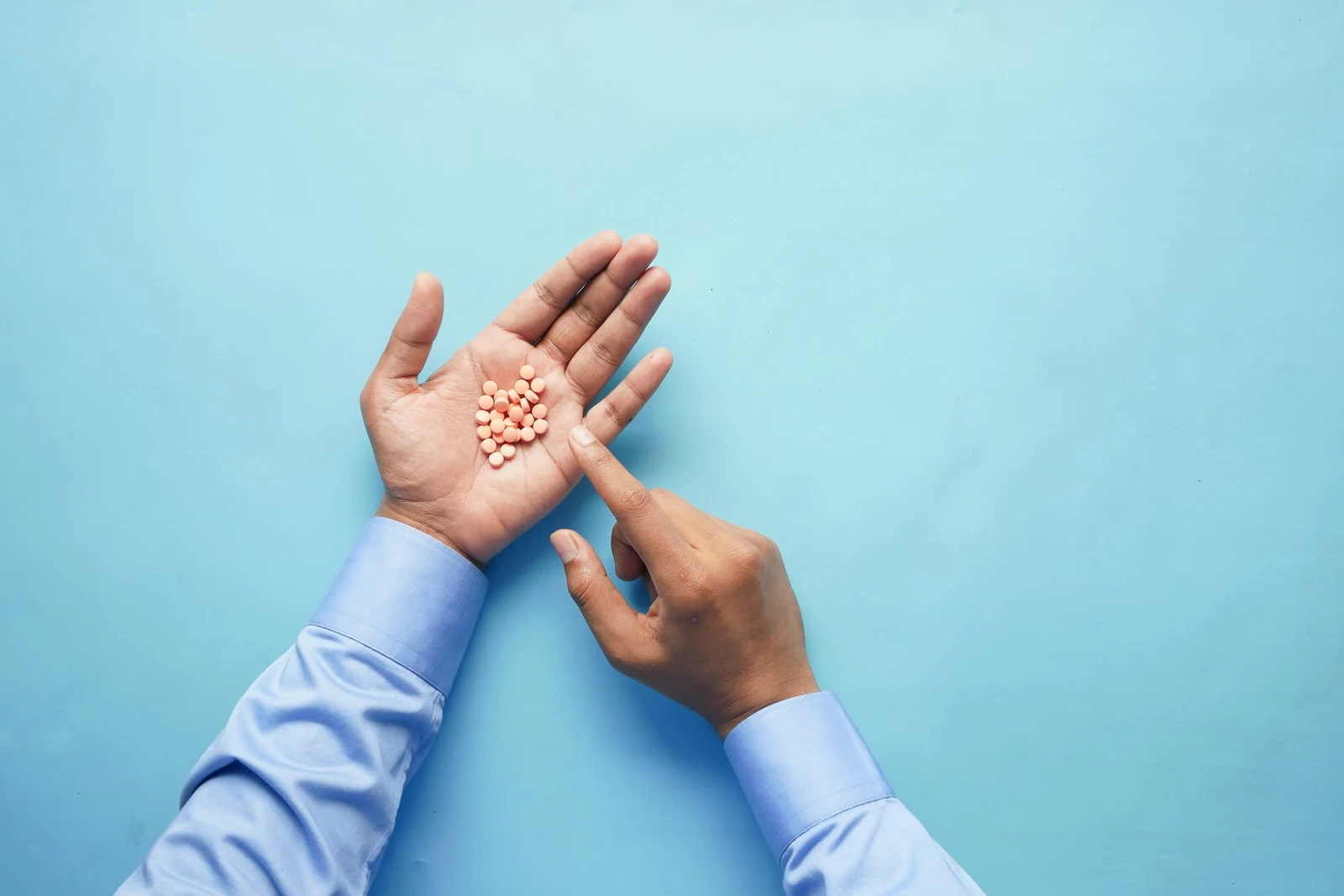 Is Gabapentin Addictive? A hand outstretched with round orange pills in its palm. Another hand reaches for a pill.